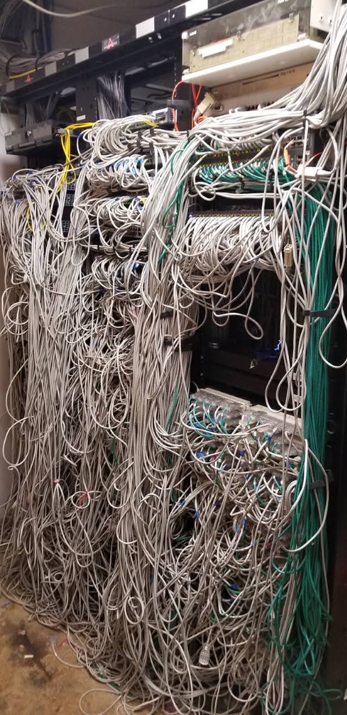 Massive tangled cabling nightmare in multi-bay commercial server rack before cleanup